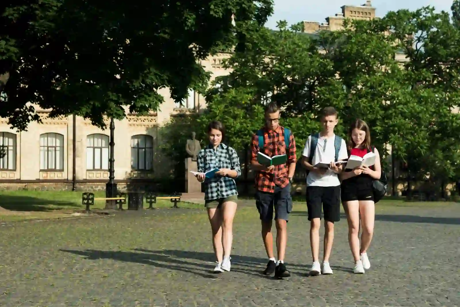 Four students walking together on a germany university campus, holding books and wearing casual clothing.