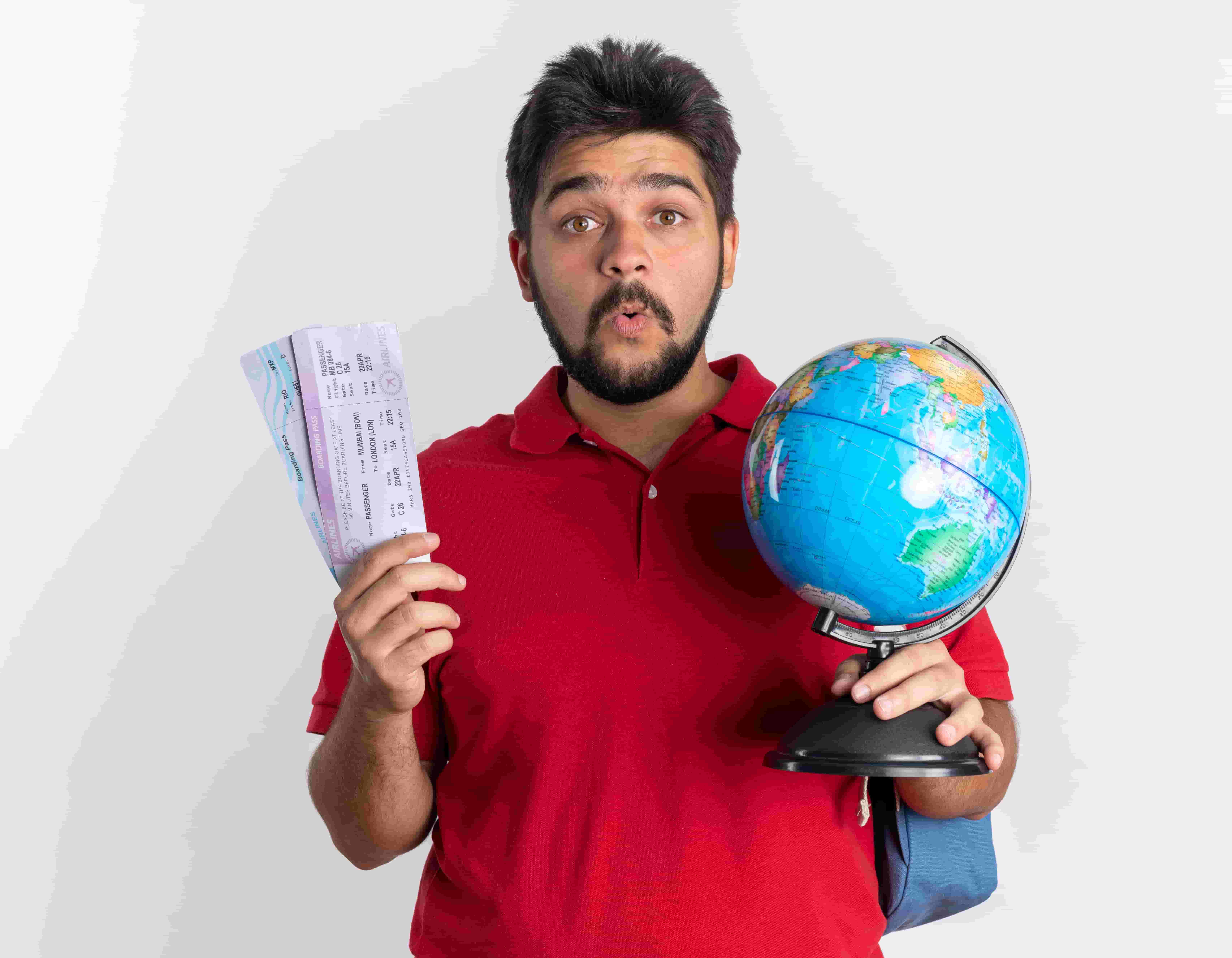 young beard student holding globe and airline tickets looking surprised